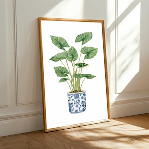 Może przedstawiać: Akwarela przedstawiająca zieloną roślinę z dużymi liśćmi w niebiesko-białym wzorzystym garnku. Grafika jest oprawiona w jasnobrązową drewnianą ramę i opiera się o białą ścianę i drewnianą podłogę.