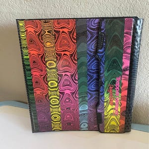 May include: A black organizer with a colorful, abstract design. The design features vertical stripes in shades of red, orange, yellow, green, blue, purple, and pink. The text "Tapperware" is visible on the side.