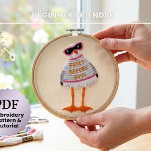 May include: An embroidery hoop with a whimsical chicken design. The chicken wears sunglasses and a striped shirt with the text "Fries Before Guys." The embroidery is set against a beige fabric, held by hands. The image also includes embroidery floss and a vase of flowers.