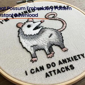 May include: A round wooden embroidery hoop containing white fabric with a stitched illustration of a grey and white opossum. The text reads I'M TRAINED IN COMBAT and I CAN DO ANXIETY ATTACKS. The opossum has a pink nose, ears, and tail.