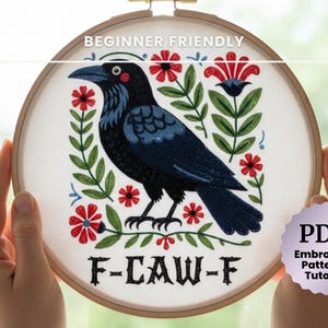 May include: Embroidery hoop featuring a black crow design with red flowers and green leaves. The text "BEGINNER FRIENDLY" is at the top, and "F-CAW-F" is at the bottom. A PDF embroidery pattern and tutorial is included.