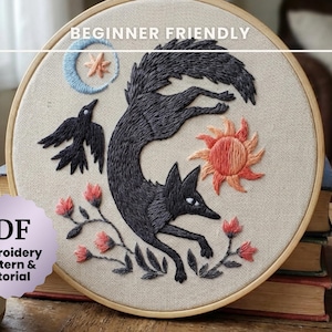 May include: Embroidered artwork in a wooden hoop features a black fox leaping across the center. A black crow, sun, moon, and flowers are also embroidered. The text "BEGINNER FRIENDLY" and "PDF Embroidery Pattern & Tutorial" are visible.
