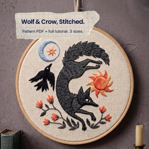 May include: A circular embroidery hoop containing a fabric panel with a stitched design of a black wolf, a black crow, a blue crescent moon, an orange star, and an orange sun, surrounded by small orange flowers. Text reads: Wolf & Crow, Stitched. Pattern PDF + full tutorial. 3 sizes.
