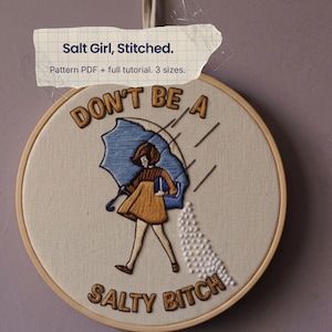 Könnte beinhalten: Ein Stickrahmen mit einem gestickten Motiv einer Person mit blauem Regenschirm und gelbem Kleid, wobei weiße französische Knoten Salz darstellen. Der Text lautet: Salt Girl, Stitched. Pattern PDF + full tutorial. 3 sizes. DON'T BE A SALTY BITCH.