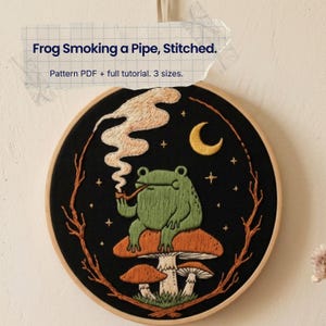 Op de afbeelding: Een ronde borduurring met een groene kikker die op een paddenstoel zit en een pijp rookt met wervelende rook, een gele maansikkel en sterren op zwarte stof. Tekst: Frog Smoking a Pipe, Stitched. Pattern PDF + full tutorial. 3 sizes.