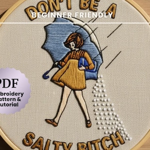 以下が含まれることがあります： 「DON'T BE A SALTY BITCH」と「BEGINNER FRIENDLY」の文字が入った刺繍枠アート。傘の下を歩く女性が描かれ、そこから塩が降っています。PDF刺繍パターンとチュートリアルが含まれています。