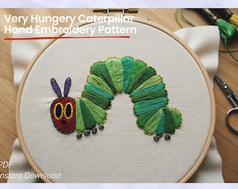 May include: Hand embroidery pattern featuring a colorful caterpillar design. The caterpillar is stitched with shades of green and red thread, set against a white fabric background within a wooden embroidery hoop. Text reads "Very Hungry Caterpillar Hand Embroidery Pattern".