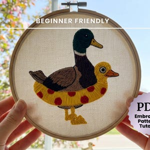 Puede incluir: Diseño de pato bordado en un aro de madera. El pato es marrón, verde y amarillo, con un salvavidas amarillo. También se ve el texto "BEGINNER FRIENDLY" y "PDF Embroidery Pattern & Tutorial".