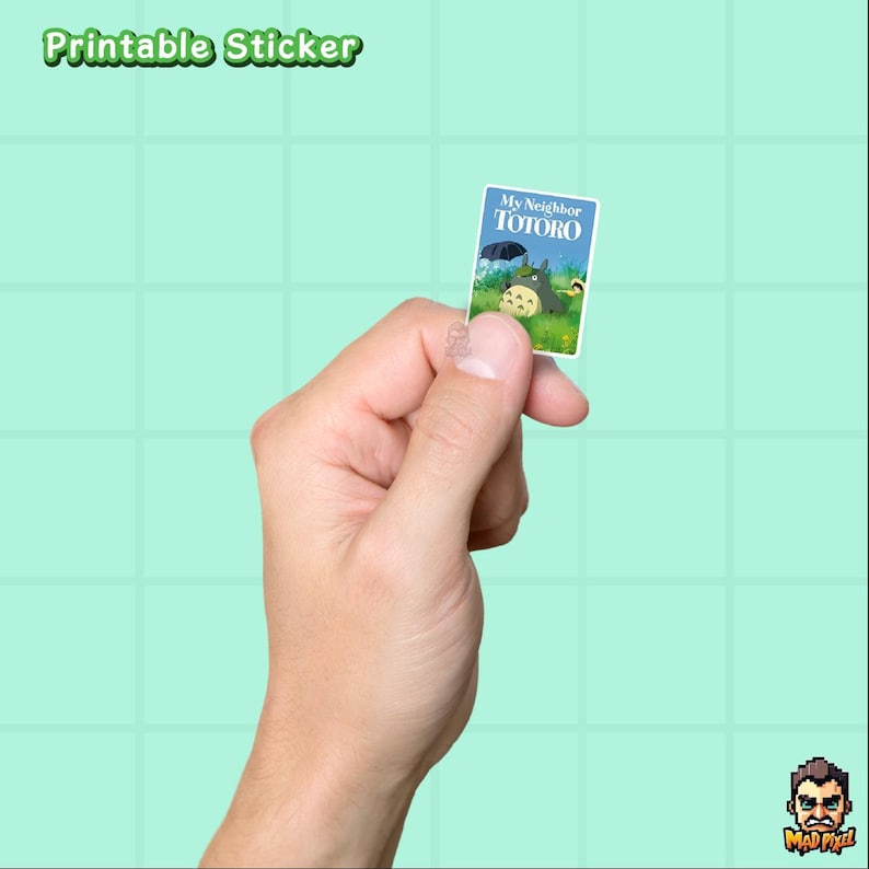 May include: A small, rectangular sticker featuring the title "My Neighbor Totoro" with an illustration of Totoro and other characters. The sticker is held between fingers against a light green background. The words "Printable Sticker" are at the top.