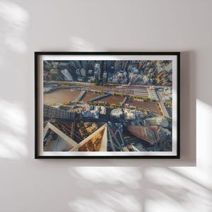 Puede incluir: Fotografía aérea de una ciudad, enmarcada en un marco negro. La imagen captura una vista de ángulo alto de edificios, un río y puentes. La composición es una mezcla de estructuras arquitectónicas y elementos naturales.