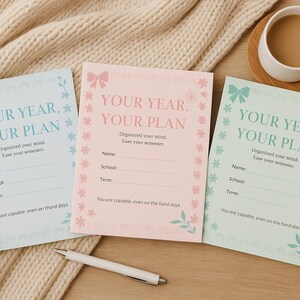 Puede incluir: Tres hojas de planificación coloridas con el texto "YOUR YEAR, YOUR PLAN". Las hojas son azul claro, rosa y verde menta, cada una con un lazo y un borde floral. También hay un bolígrafo blanco y una taza de café.