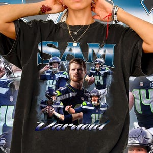 Puede incluir: Camiseta negra con un collage de un jugador de fútbol americano con uniforme azul y verde. La camiseta tiene los nombres "SAM" y "Vorrla" impresos. La camiseta es de estilo vintage.