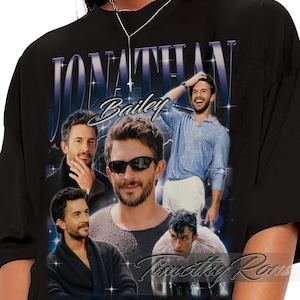 May include: Black t-shirt featuring a collage of images of Jonathan Bailey, with the name "Jonathan Bailey" in a stylized font. The shirt has a vintage, retro design with a light blue and white color scheme.