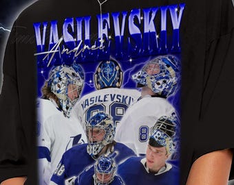 Puede incluir: Camiseta negra con un collage azul y blanco de imágenes de porteros de hockey. El nombre "Vasilevskiy" y "Andrei" se muestran en una fuente azul estilizada. El diseño incluye gráficos de rayos.