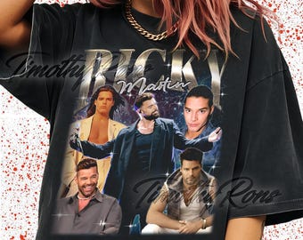 May include: Black t-shirt featuring a graphic of Ricky Martin with the text "Ricky Martin" in a silver metallic font. The design includes multiple images of the singer. The shirt has a vintage, distressed look.