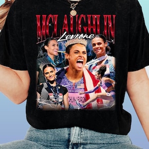 May include: Black t-shirt with a collage of images of Sydney McLaughlin-Levrone, a track and field athlete. The design includes her name in red, with additional text and images of her competing.