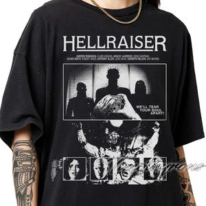 May include: Black t-shirt featuring the movie title "HELLRAISER" in white block letters above a black and white graphic. The graphic includes images of characters and the text "WE'LL TEAR YOUR SOUL APART!" The names of the actors are listed below the title.