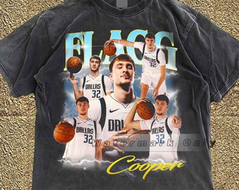 Puede incluir: Camiseta gris oscuro con un jugador de baloncesto, la palabra "FLAGG" en azul claro y el nombre "Cooper" en amarillo. El jugador lleva una camiseta blanca con "DALLAS 32". La camiseta tiene un aspecto vintage y desgastado.