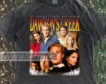 Puede incluir: Camiseta gris oscuro con el texto "DAWSON'S CREEK" en degradado amarillo y naranja. La camiseta muestra una foto grupal del elenco. La camiseta está hecha de un material suave.
