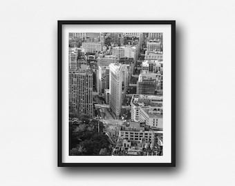 May include: Black and white framed print of a cityscape, featuring tall buildings and streets. The iconic Flatiron Building is prominently displayed. The photograph is taken from an aerial perspective, showcasing the urban landscape.