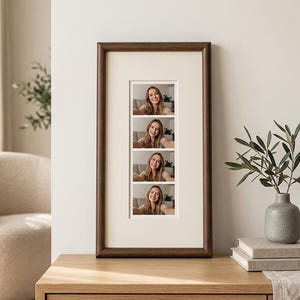 Op de afbeelding: Een verticale rechthoekige fotolijst van donker hout met een crèmekleurige passe-partout. De lijst bevat een strook van vier identieke vierkante foto's van een glimlachend persoon met lang haar, gerangschikt in één enkele kolom.