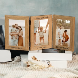 May include: A wooden triple photo frame with three hinged panels. Each panel displays a family photo with the phrases "Forever love", "I love you", and "We are family" etched at the bottom. The frame is made of light-coloured wood.