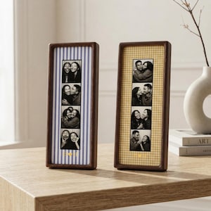 Può includere: Due cornici rettangolari in legno scuro posizionate in verticale. La cornice a sinistra presenta uno sfondo a righe blu e bianche con una striscia verticale di quattro foto in bianco e nero e il testo dorato H+H. La cornice a destra ha uno sfondo a quadretti vichy gialli.