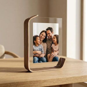 May include: A vertical photo frame featuring a curved, light-brown wooden base and frame structure that holds a clear acrylic panel. The panel displays a photograph of a family of four, including two adults and two children, smiling together.