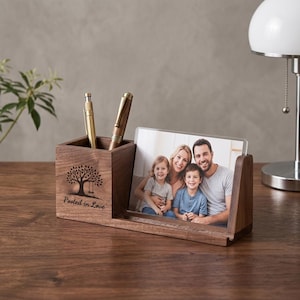 Peut inclure: Un organiseur de bureau en bois avec un porte-stylo et un cadre photo. Le porte-stylo présente un motif d'arbre et les mots "Rooted in Love". Le cadre photo contient un portrait de famille. L'organisateur est en bois foncé.