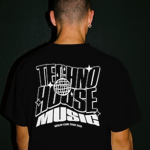 May include: Black t-shirt with a white graphic design. The design features the words "TECHNO HOUSE MUSIC" in a stylized font, with a globe and star accents. The text "BERLIN CLUB TOUR 2025" is below the main text.
