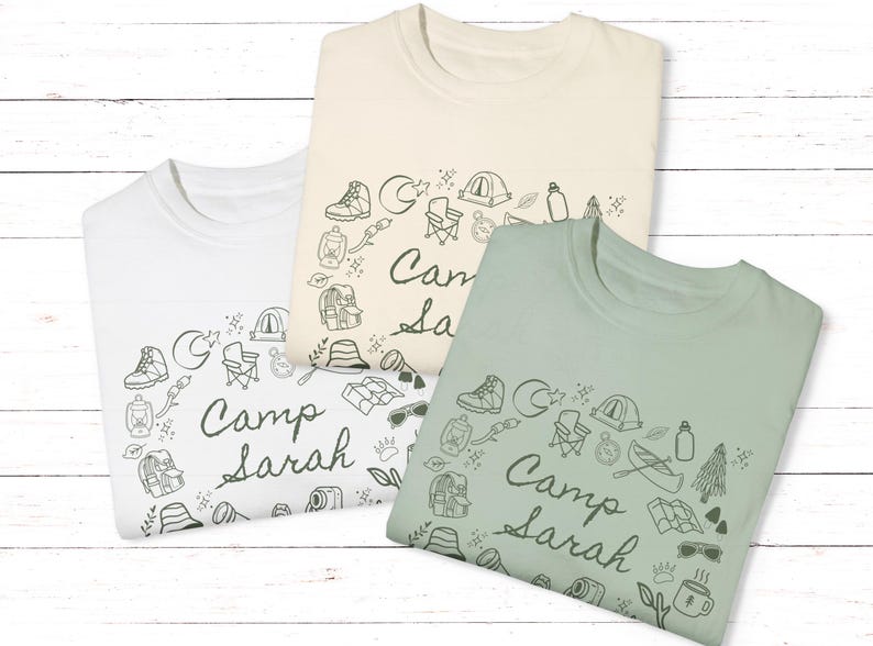 May include: Three t-shirts with a camping theme. The shirts are white, beige, and green. Each shirt has a circle of camping-related illustrations and the text "Camp Sarah".