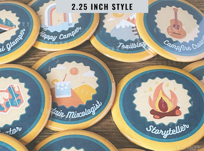 May include: A collection of round pin-back buttons, each 2.25 inch style, featuring various camping-themed illustrations and text including Happy Camper, Trailblazer, Campfire Crooner, Mountain Mixologist, and Storyteller in blue and yellow.