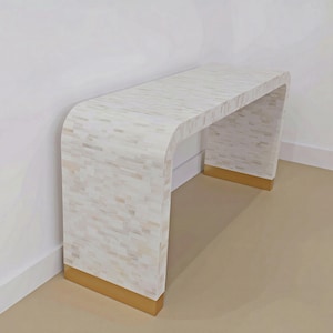 Op de afbeelding: Een waterval-console-tafel met een oppervlak van witte en crèmekleurige tegelinleg met een rechthoekig patroon. De basis van de tafel is afgewerkt met metallic goudkleurige accenten aan beide zijden, wat een contrast vormt met het lichte blad.