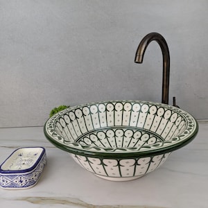 May include: A white ceramic sink with a green and black decorative pattern and a matching soap dish. The sink has a dark bronze tap. The sink and soap dish are on a white surface.