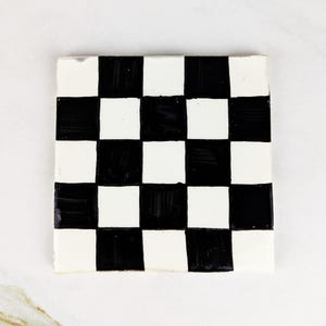 Puede incluir: Posavasos cuadrado a cuadros blancos y negros. El posavasos presenta un patrón de tablero de ajedrez clásico con cuadrados blancos y negros alternados. El diseño es simple y gráfico, adecuado para varios estilos de decoración.