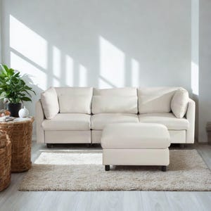 May include: A cream-colored sectional sofa with matching ottoman sits on a shaggy rug. The sofa has three sections with large, square cushions and pillows. A potted plant and woven side tables are on the left.