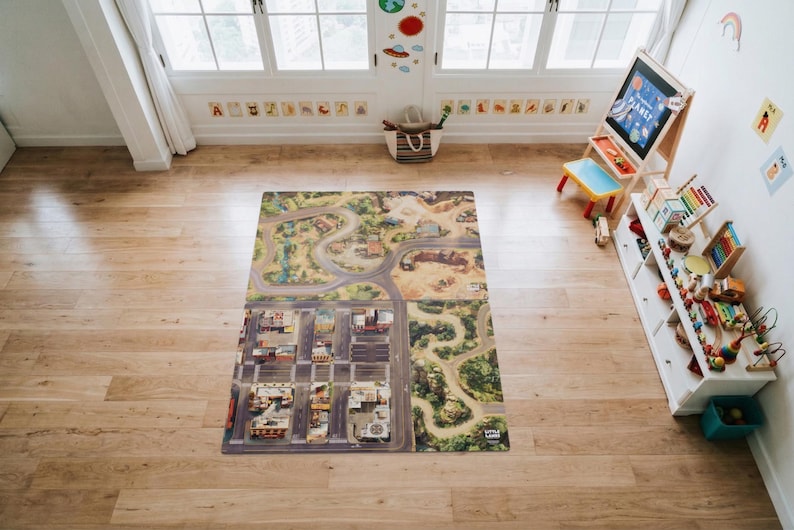 May include: A rectangular play mat featuring a detailed printed map with a city grid, winding roads, and natural landscapes. The mat displays various buildings, parking lots, and green areas, providing a surface for imaginative play activities.
