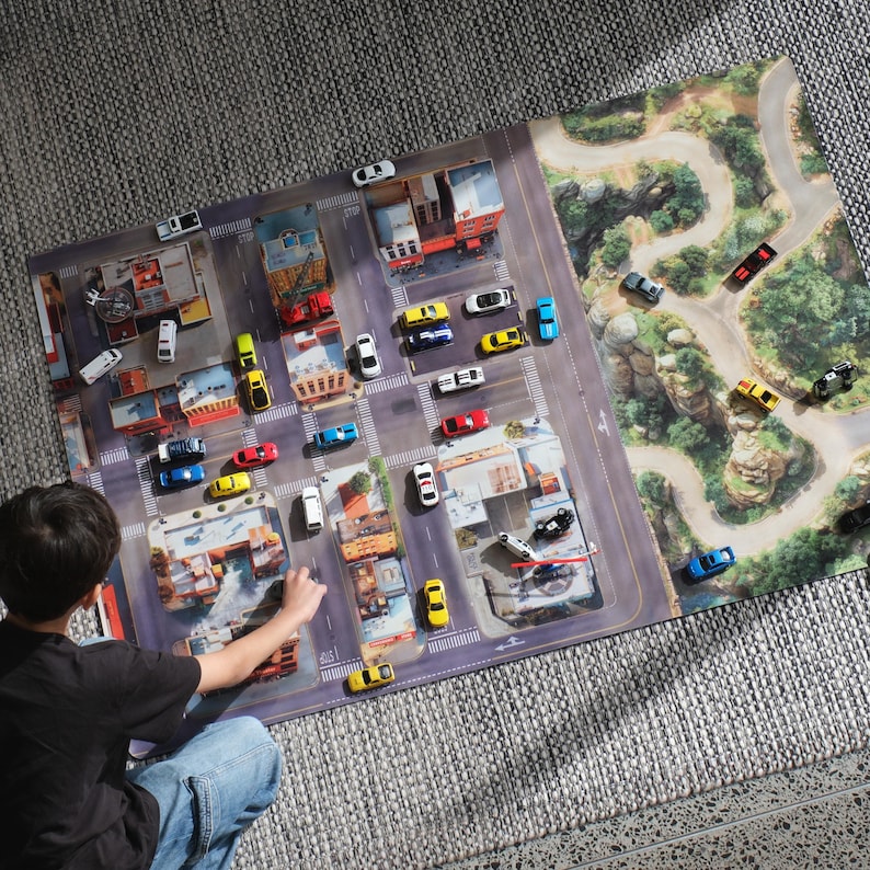 May include: A rectangular play mat featuring a printed city street grid on the left and a winding mountain road on the right. Numerous small toy cars in various colours are positioned across the urban and natural landscape illustrations.