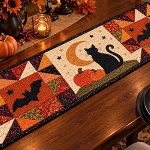 May include: A rectangular quilted table runner featuring a patchwork design with Halloween motifs. The fabric displays black bats, a black cat, orange pumpkins, and a crescent moon against a background of autumn-colored geometric patterns.
