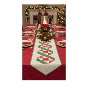 Könnte beinhalten: Eine festliche Weihnachts-Tischdekoration mit roter Tischdecke und einem weiß-grünen, gesteppten Tischläufer. Der Läufer hat ein sich wiederholendes Muster aus roten und grünen Formen. Ein Kerzen-Mittelstück und Gedecke vervollständigen die Szene.