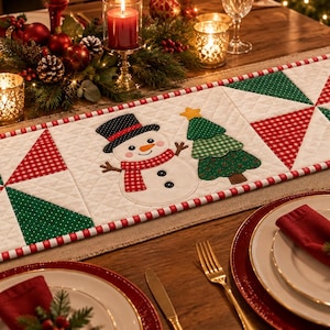 Puede incluir: Un camino de mesa acolchado rectangular con una aplicación central de un muñeco de nieve con sombrero negro y bufanda roja junto a un árbol de Navidad verde. El camino presenta patrones geométricos de molinillo rojos y verdes.