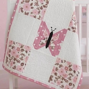 May include: A patchwork quilt featuring alternating squares of white fabric with quilted swirling patterns and floral fabric with pink flowers and brown leaves. A central butterfly applique has pink wings with white hearts and a solid black body.
