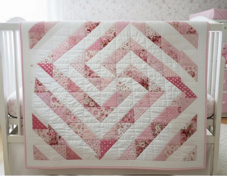 May include: A baby quilt with a geometric design in shades of pink and white. The quilt features a repeating pattern of triangles and squares, with floral and polka dot accents. The quilt is displayed on a white crib.