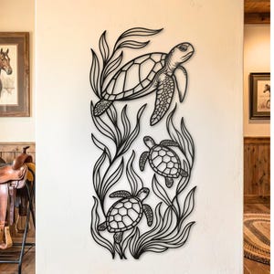 May include: Black metal wall art featuring three sea turtles swimming among stylized seaweed. The turtles have detailed shell patterns and are depicted in a naturalistic style. The artwork is mounted on a white wall, creating a striking contrast.
