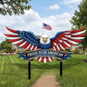 Puede incluir: Un letrero de jardín patriótico con un águila calva americana estilizada con las alas extendidas, pintada en rojo, blanco y azul. El letrero dice "PROUD TO BE AMERICAN" y celebra 250 años. Una bandera estadounidense ondea en el fondo.