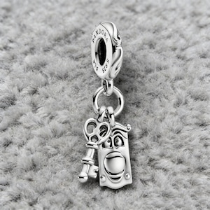 May include: A silver charm with a key and a door knocker design. The charm is suspended from a ring and has the word "Pandora" engraved on the top. The door knocker has a smiling face.