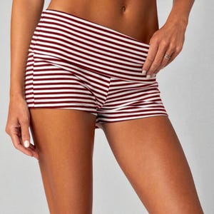 May include: Close-up of striped shorts. The shorts feature horizontal stripes in burgundy and white. The waistband is folded over. The shorts are made of a soft, stretchy material. The shorts are designed for comfort and style.