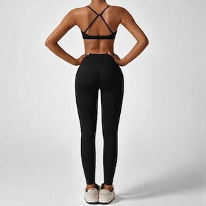 May include: Black athletic leggings and a matching sports bra with crisscross back straps. The activewear set is made of a stretchy material and is designed for workouts. The model is wearing white sneakers.