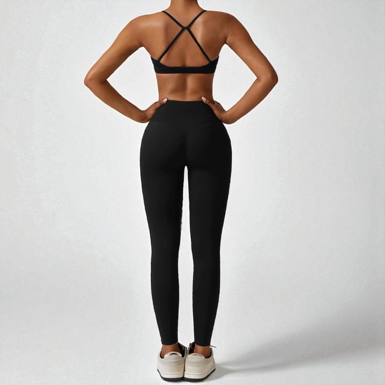 May include: Black athletic leggings and a matching sports bra with crisscross back straps. The activewear set is made of a stretchy material and is designed for workouts. The model is wearing white sneakers.