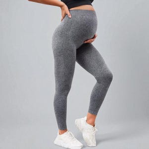 May include: Grey maternity leggings with a ribbed texture. The leggings are designed for comfort and support during pregnancy. The model is wearing white trainers and a black top.